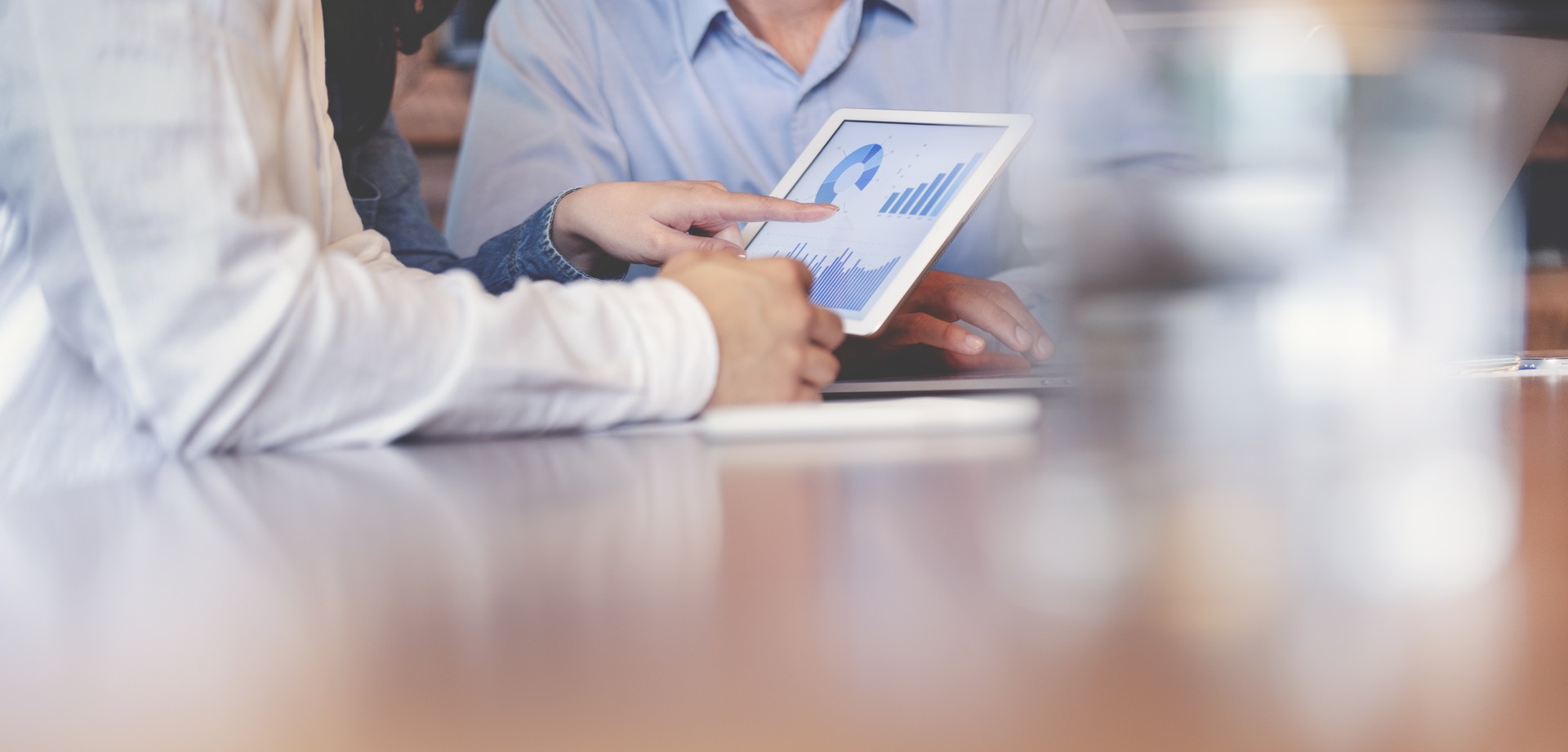 Personen schauen auf ein Tablet, auf dem verschiedene Grafiken angezeigt werden